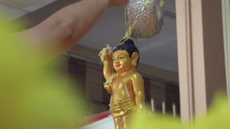 a devotee pours water over a golden baby buddha statue during the vesak day ritual, symbolizing purification and reverence in a traditional buddhist ceremony.