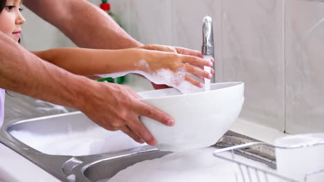 a father is teaching his daughter to wash the dishes