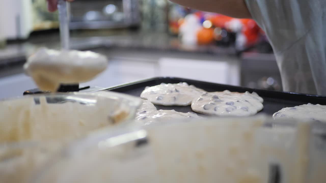 Woman scoops chocolate chip pancake batter onto pan in slow motion