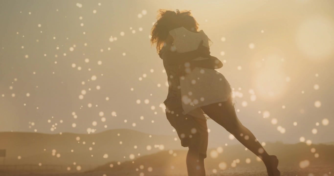 Mand løfter kvinde på klitter, drejer, krammer og går, med bokeh-effekt der overlejrer former, til romantiske reklamer.