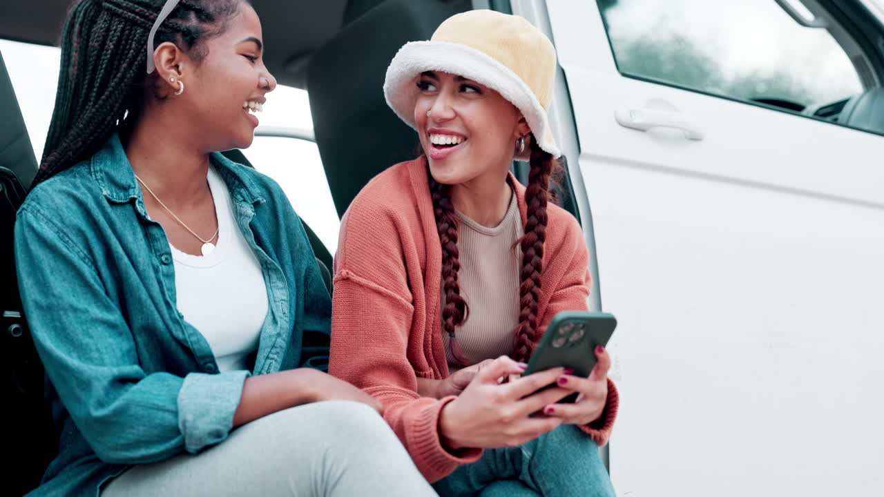 Two friends on a road trip sitting near a van looking at a phone