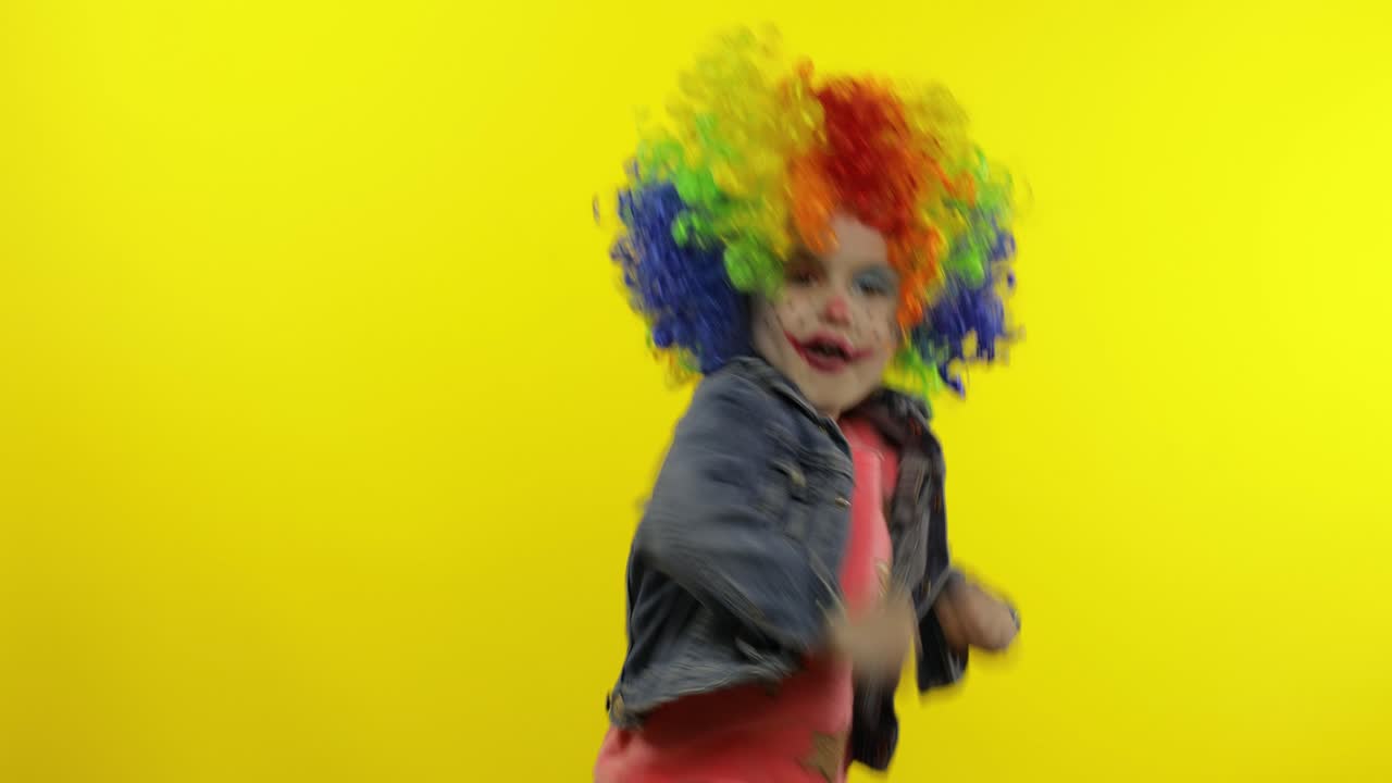 una niña payasa con una peluca colorida haciendo caras tontas. divirtiéndose, sonriendo, bailando. halloween