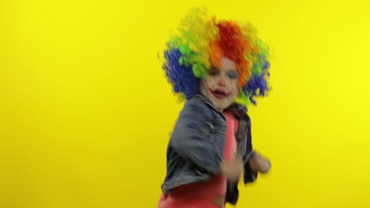 Bambina pagliaccio con una parrucca colorata che fa facce buffe. Si diverte, sorride, balla. Halloween