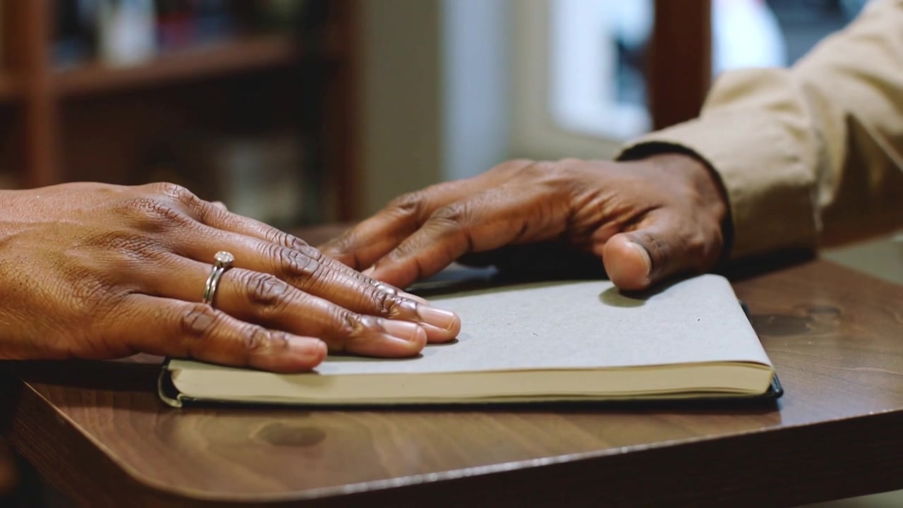 Hovering right hand beige cuff moving bookmark on gray notebook on wood table left hand rings