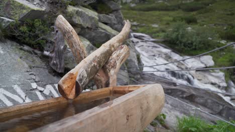 Una-Fuente-De-Madera-Con-Agua-Potable-Junto-A-Un-Río-En-Los-Alpes-Austriacos