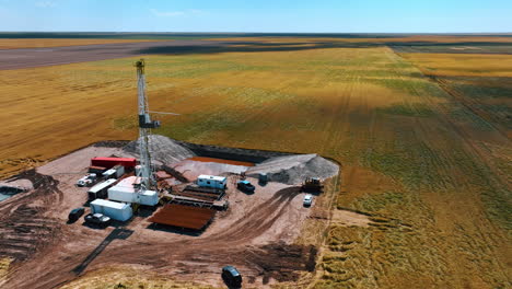 approaching the oil production site in the immense field. derrick in the center of location, equipment for drilling resources, two water pools and cars around the rig.