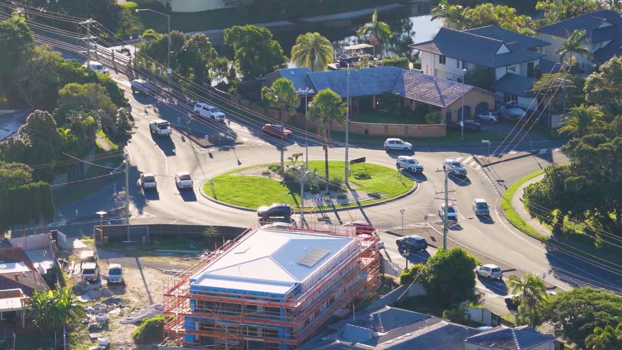 Aerial footage captures cars navigating a busy roundabout in Gold Coast, Australia, under bright daylight, showcasing urban traffic flow