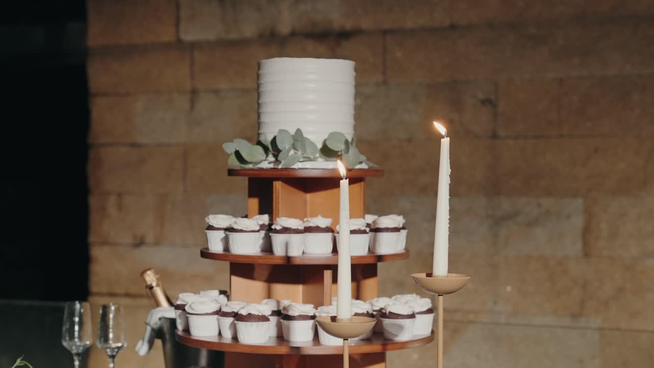 Bánh cưới và bánh cupcake được sắp xếp trên giá gỗ với nến đang cháy.