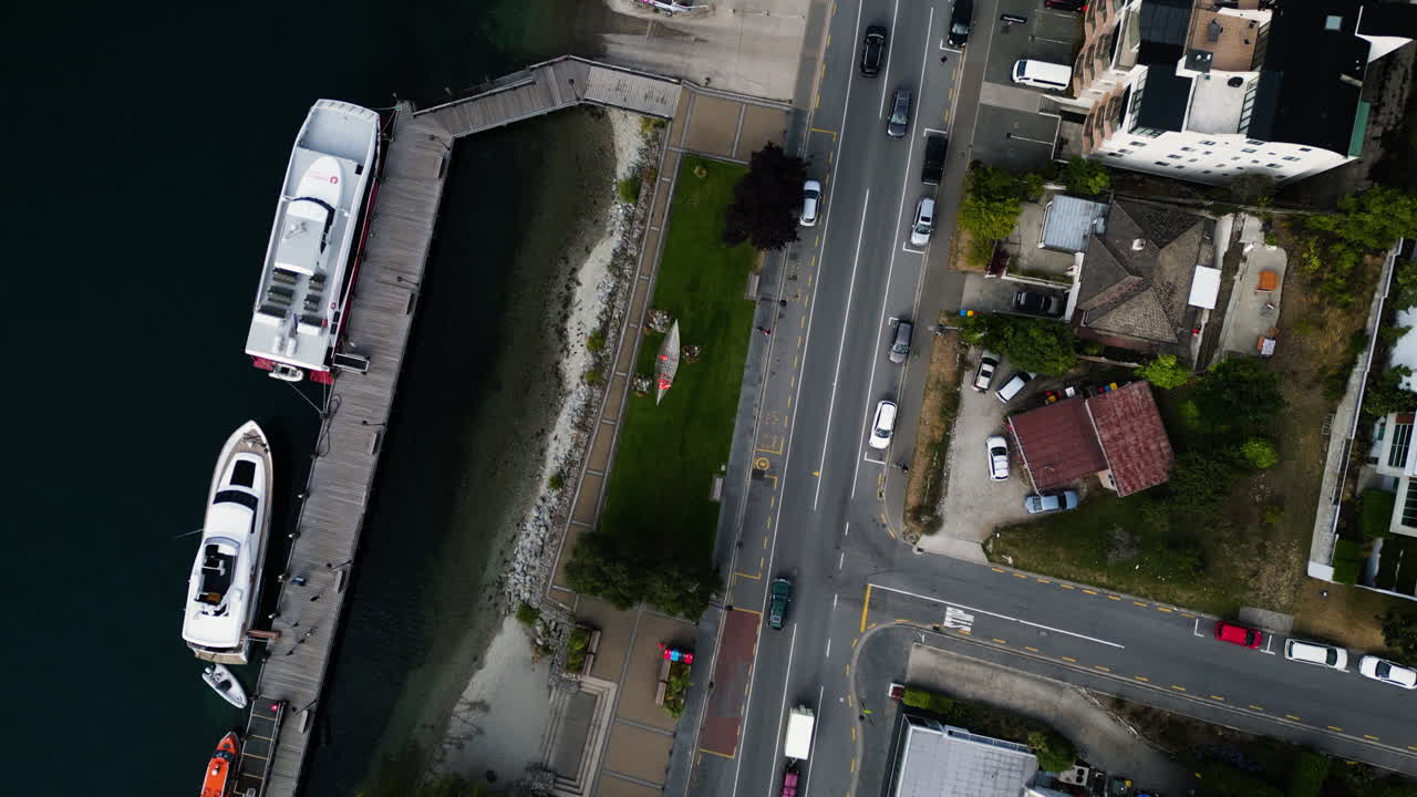 aéreo de arriba hacia abajo de queenstown, drones de nueva zelanda vuelan sobre la concurrida calle de tráfico y la costa con un velero amarrado en el muelle
