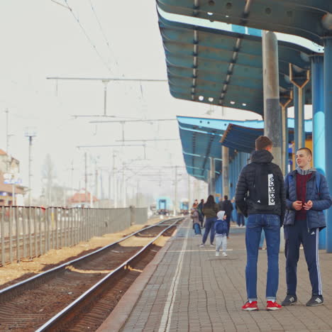 two teenagers standing on a railway platform waiting for a train. young men in sportive clothes talking to each other on a railway station outdoors.