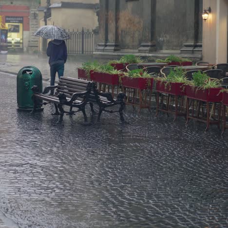 a man with an umbrella in his hand is passing the summer terrace of a restaurant in the street in rainy weather.
