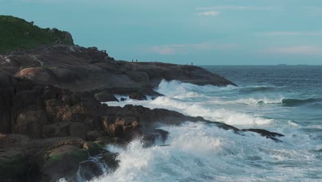 Siluetas-De-Personas-De-Pie-Sobre-Rocas,-Contemplando-El-Hermoso-Mar,-Donde-Las-Olas-Rompen-Contra-La-Escarpada-Costa