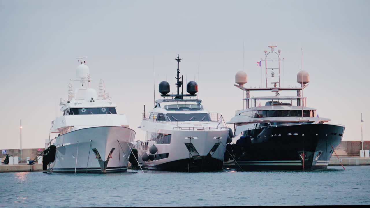 Tre yacht di lusso ormeggiati uno accanto all'altro in un porto turistico tranquillo, ripresi con una luce diurna soffusa