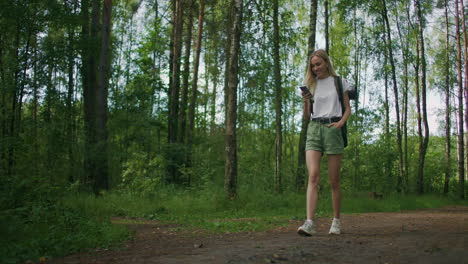 general plan mobile phone in the hands of a female traveler walking through the forest. social networks navigator and messenger. use your mobile phone for a walk in the woods