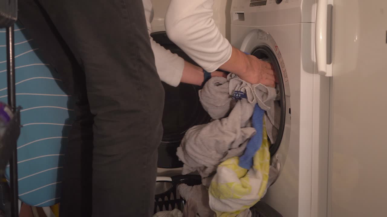 el joven trae una cesta de ropa y mete una lavadora de carga frontal