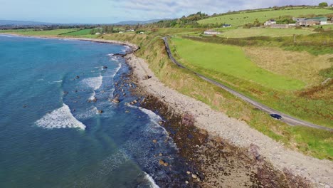 descending aerial view of waves, rocky shoreline and costal road along the south coast of ireland