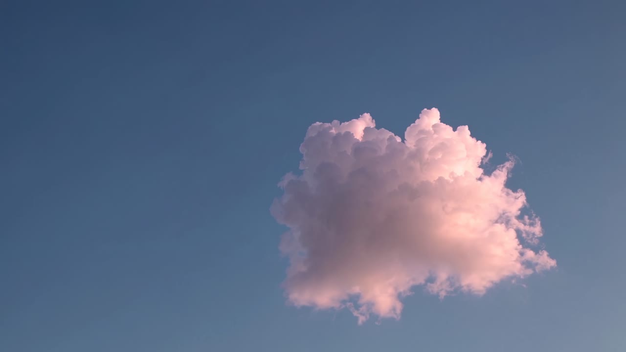 A single fluffy cloud against a clear blue sky, captured from a low angle