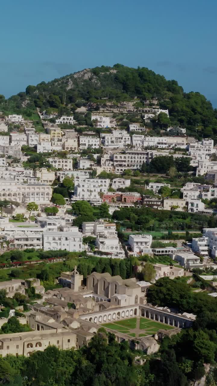 Vertical Drone View Flying Towards a Famous Travel Destination Town in Capri Island with White Buildings Located on Top of Italy's Most Renowned Rocky Limestone Island in the Mediterranean Sea