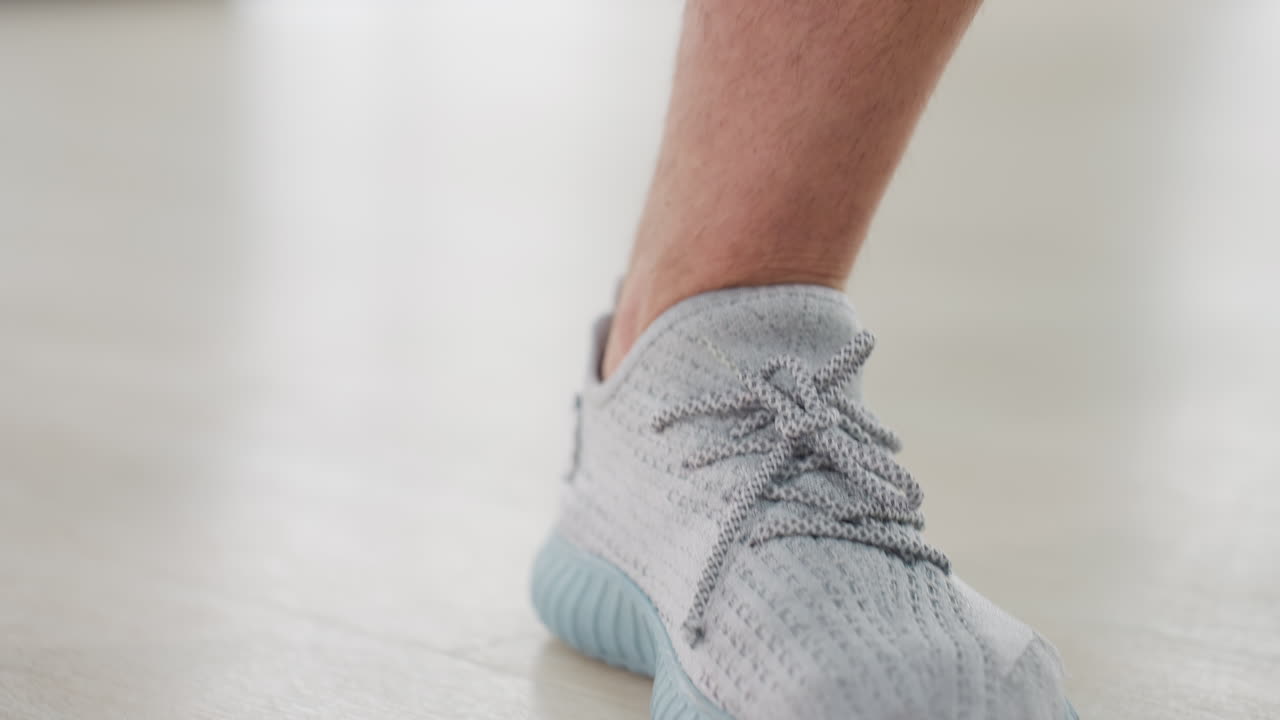 Muscular man pressing thigh during deep side lunge exercise in gym studio with large floor to ceiling windows overlooking cityscape on light wooden floor wearing white tank top and black shorts