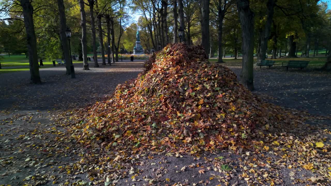 Large colorful pile of autumn leaves in Humlegården park, Stockholm, surrounded by trees