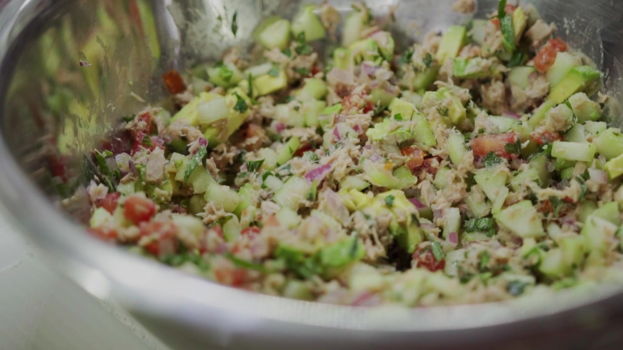 Closeup view of tuna ceviche mixed with chopped avocado, vegetables and herbs inside metal bowl, colorful ingredients highlighting fresh seafood meal and homemade food preparation