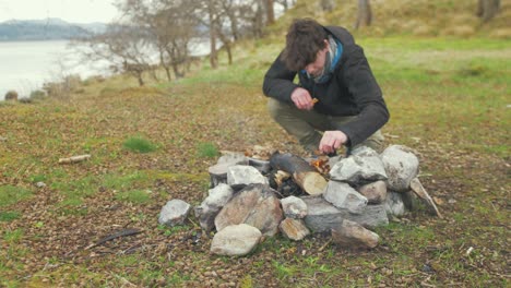 Campfire-young-man-on-island-gently-adds-leaves-and-kindling-to-fire