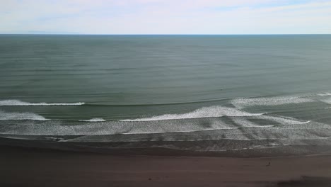 Single-person-walking-along-black-sand-beach-in-Raglan,-New-Zealand