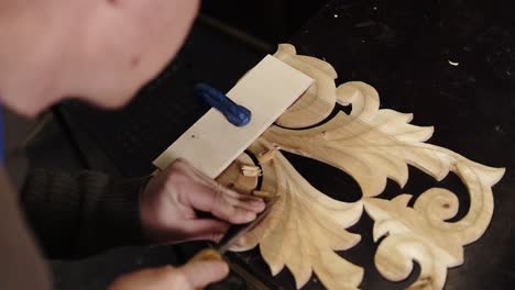 carpenter working on a wooden in his workshop on the table, preparing a detail of wooden product, a part of future furniture. high angle view of a man cuts out patterns with a planer