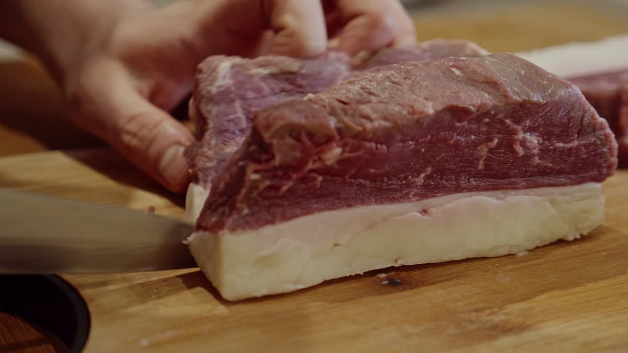 Affettare la bistecca con un coltello da cucina in acciaio contro la fibra su un tagliere di legno