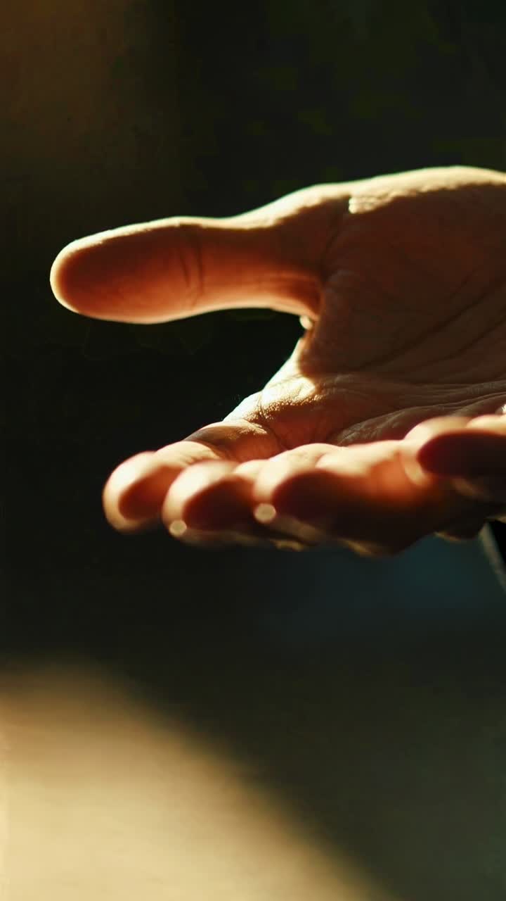Fermo immagine video in primo piano di una mano aperta, con il palmo verso l'alto, e un'illuminazione drammatica