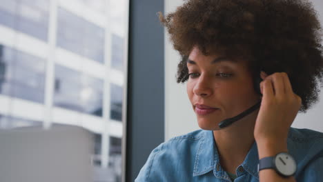 Junge-Geschäftsfrau-Im-Modernen-Büro,-Die-Mit-Einem-Drahtlosen-Headset-Am-Laptop-Arbeitet