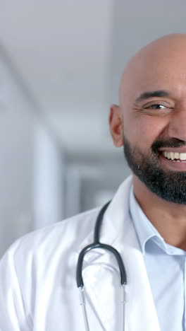 vertical video of portrait of happy biracial male doctor wearing stethoscope, slow motion