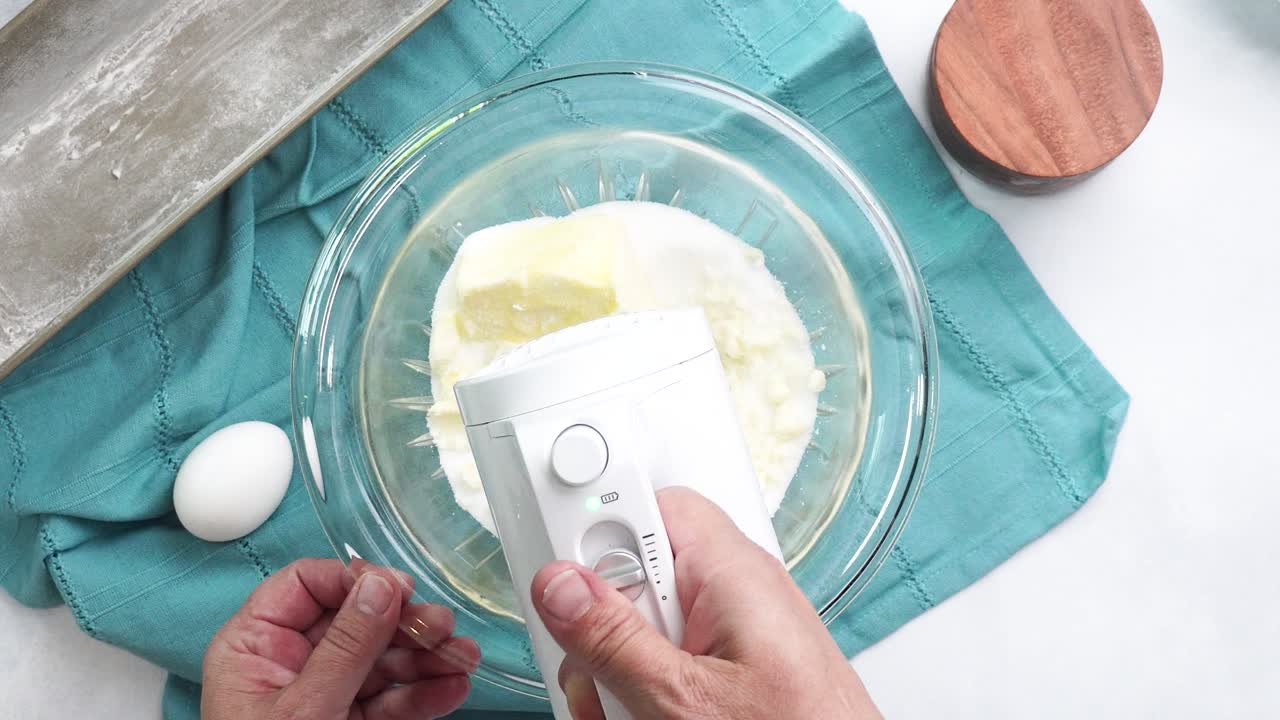 Making a dessert called Red Raspberry Tea Cake made with fresh berries and vanilla buttercream frosting. Great for Tea Parties. Using a white electric handheld mixer to combine butter into the batter