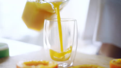 Woman-pouring-orange-juice-from-glass-jar-into-glass.-Close-up-glass