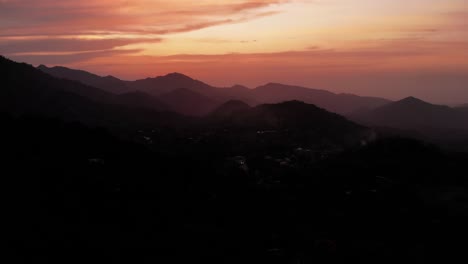 Fiery-red-sunset-over-dark-silhouette-mountain-range-in-Colombia,-aerial-tilt-up