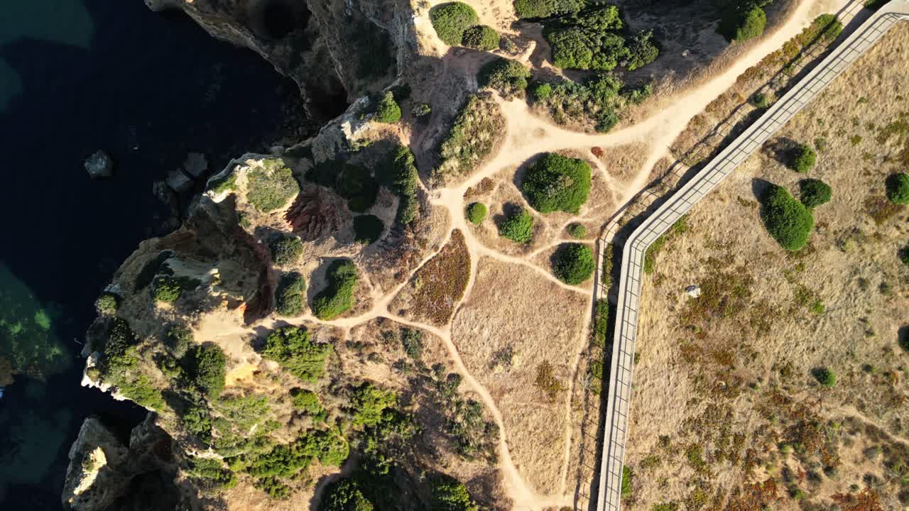 Top-down drone view of winding trails and rocky terrain with cliffs and clear sea at Ponta da Piedade in Lagos, Algarve, Portugal showing natural textures and coastal landscape from above