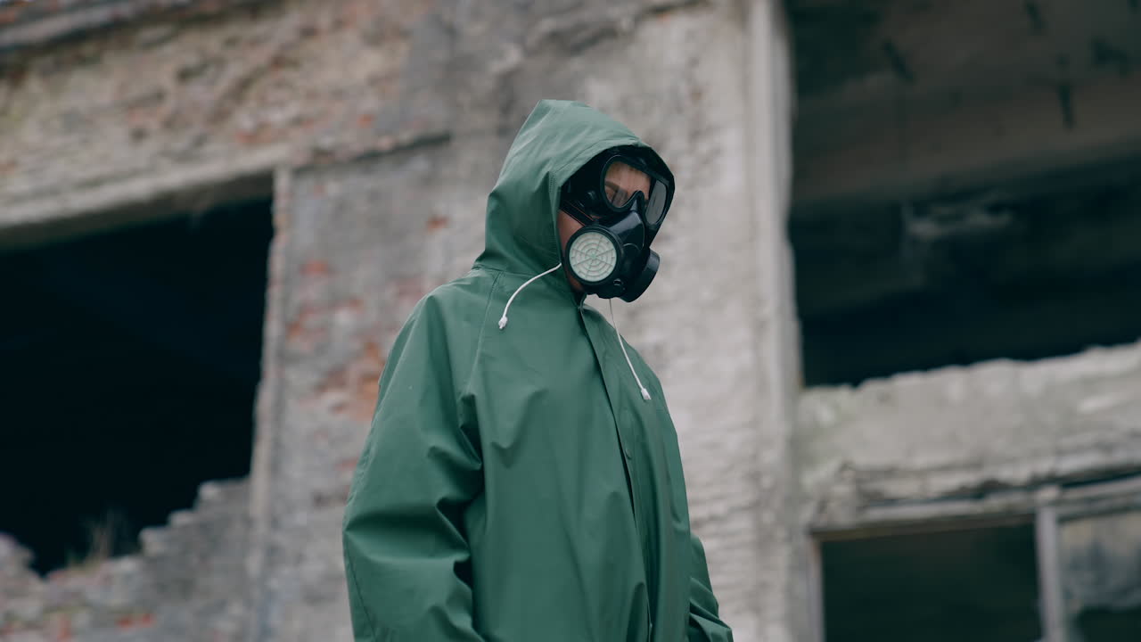 Unrecognizable person in safety suit and respirator. Human wearing hazmat suit looking for somebody on the background of destroyed building. Chemical attack.