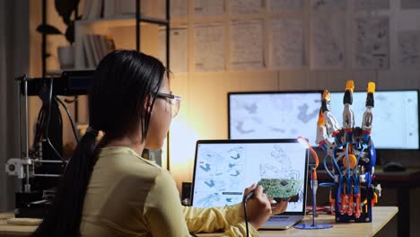 back view of teen asian girl holding and fixing the circuit board while repairing a cyborg hand at home