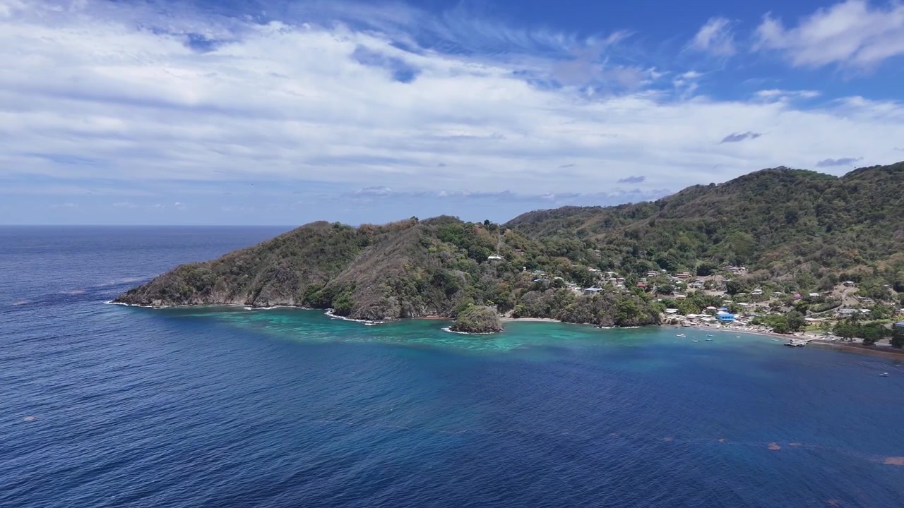 Ripresa aerea cinematografica della costa montuosa a Speyside, Isola di Tobago. Acque limpide e turchesi della baia che incontrano rigogliose colline tropicali sotto un cielo drammatico a Trinidad e Tobago, Caraibi.