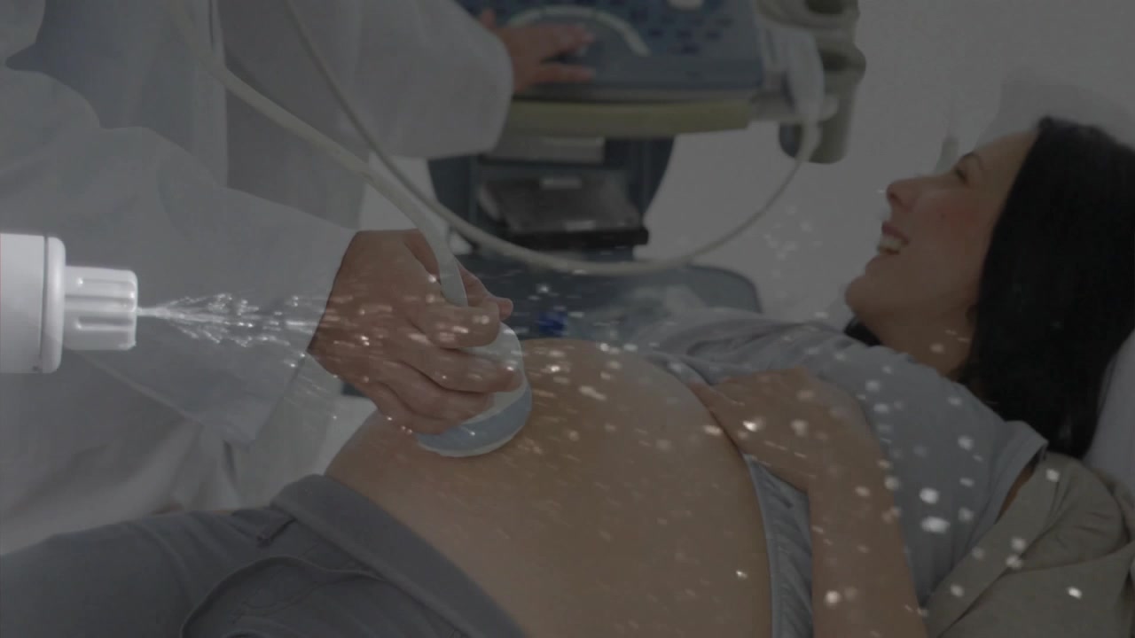 Operatore sanitario che applica gel per ecografia sull'addome di una donna incinta e utilizza la sonda mentre regola la console.