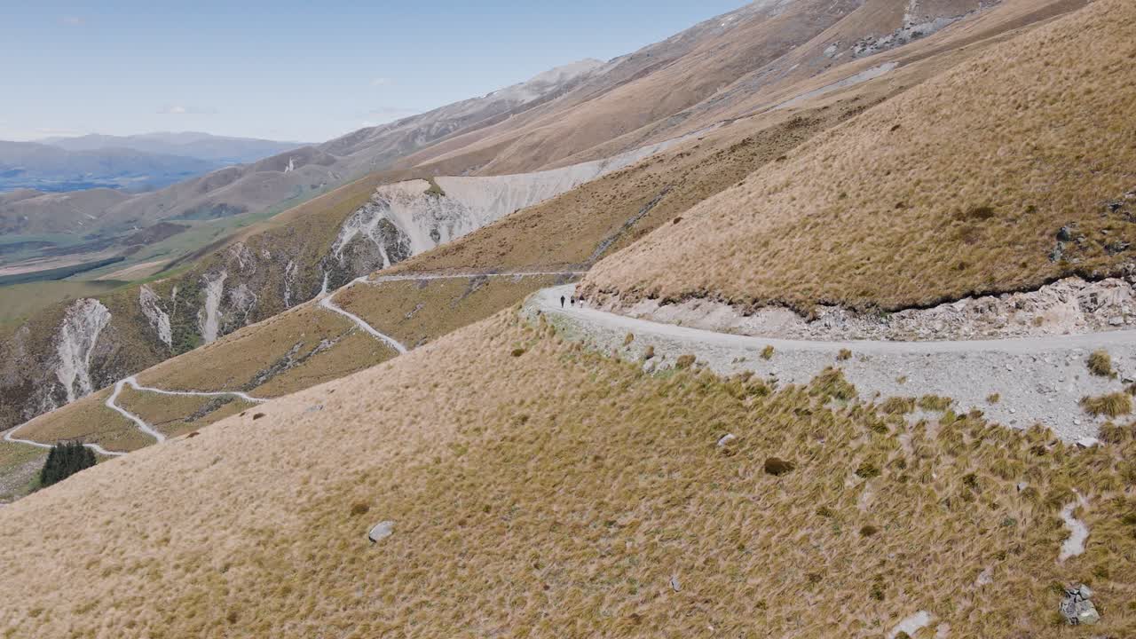 tussock ladera de la montaña cubierta de hierba con un estrecho camino de tierra que conduce a mackenzie, nueva zelanda