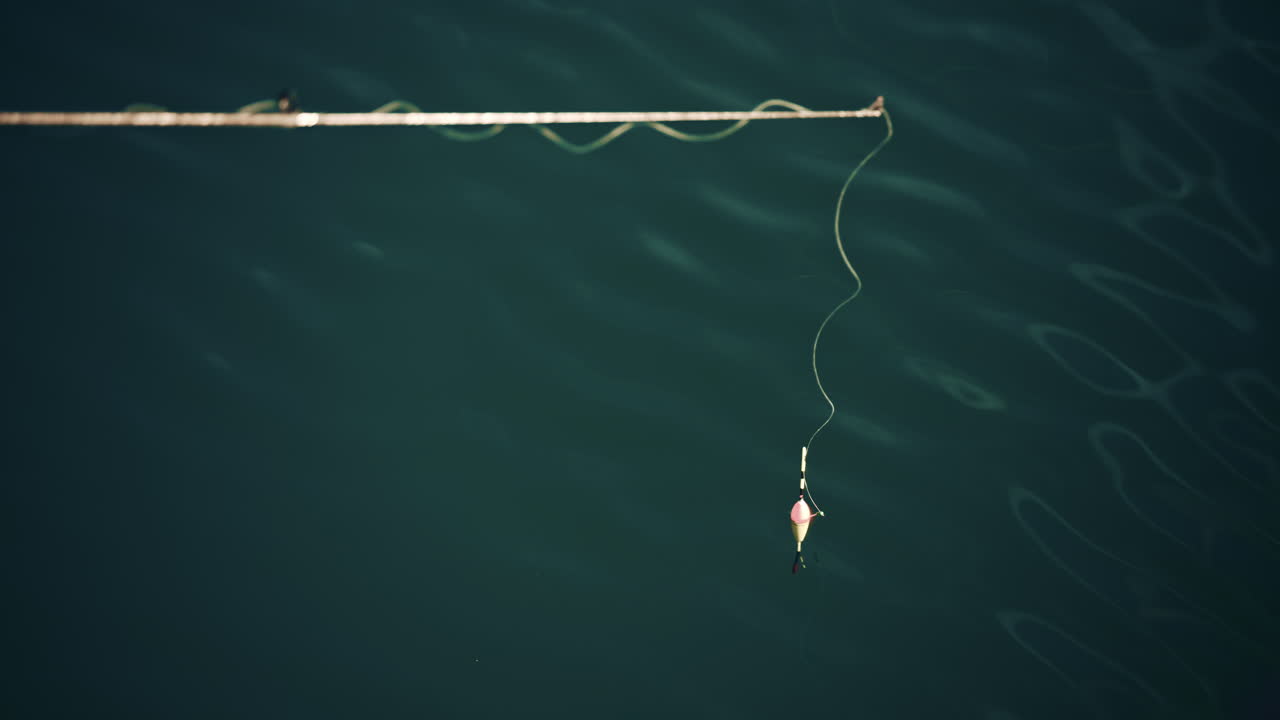 A fishing line and float gently drifting on dark water, minimal and serene