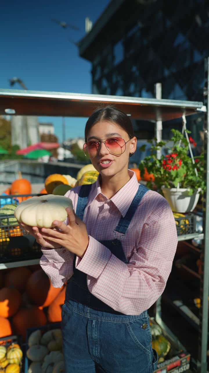 una mujer joven en el mercado de un granjero mirando una calabaza