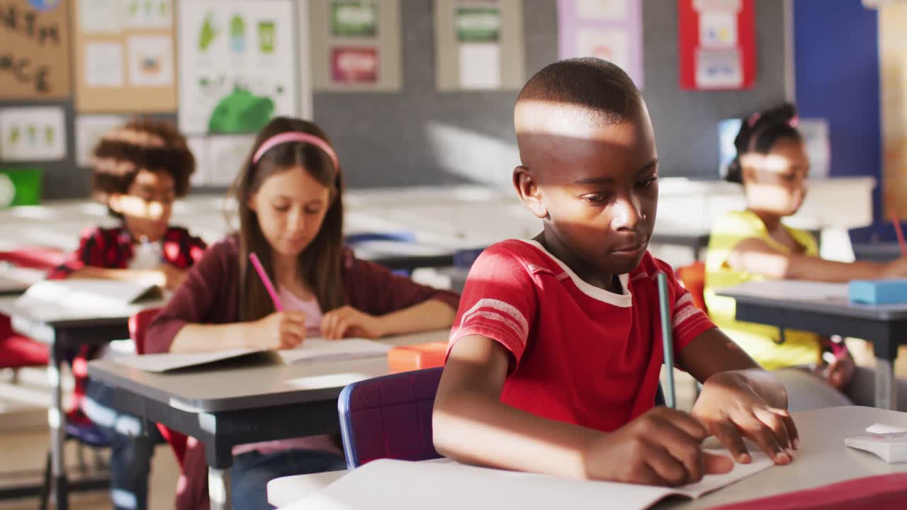 Portrait of african american schoolboy sitting in class, making notes, looking at camera