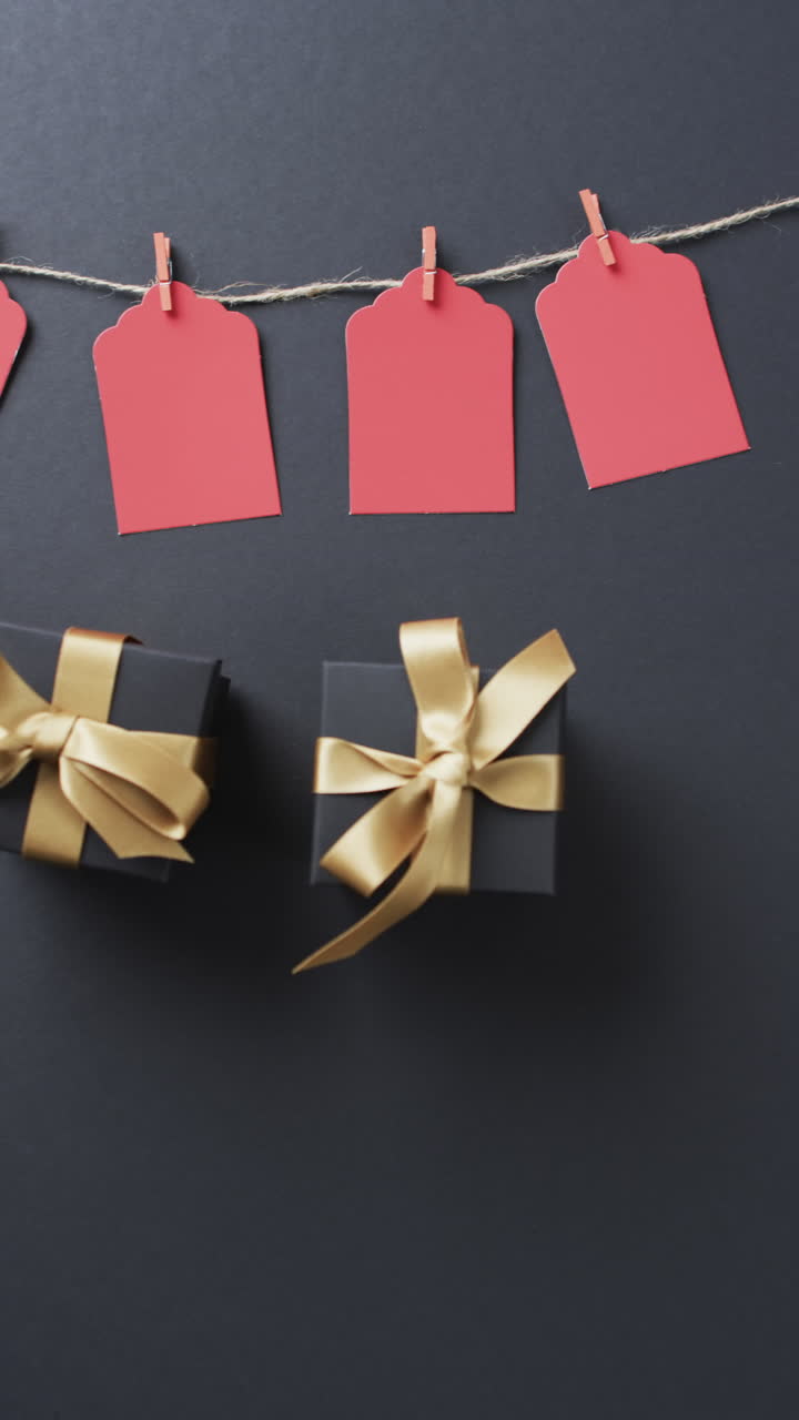 Vertical video of gift tags on string, gift boxes with ribbons and copy space on black background