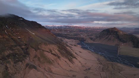 Vista-Aérea-Del-Paisaje-De-Un-Río-Que-Fluye-Desde-Un-Valle-De-Montaña,-En-Islandia,-En-Una-Tarde-Nublada