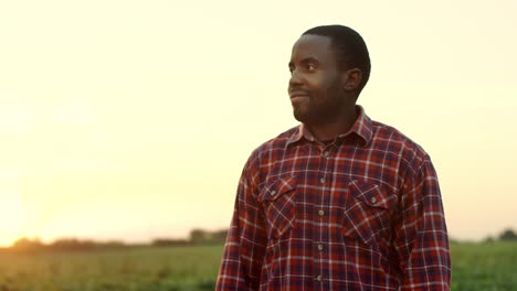 Retrato-Del-Apuesto-Joven-Agricultor-Parado-En-El-Campo-Al-Atardecer,-Sonriendo-A-La-Cámara-Y-Cruzando-Las-Manos-Frente-A-él