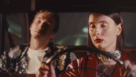woman driving vintage car at night with male passenger in back seat