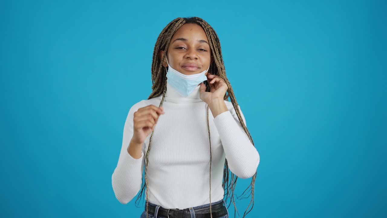 A young Black woman puts on a medical face mask for protection
