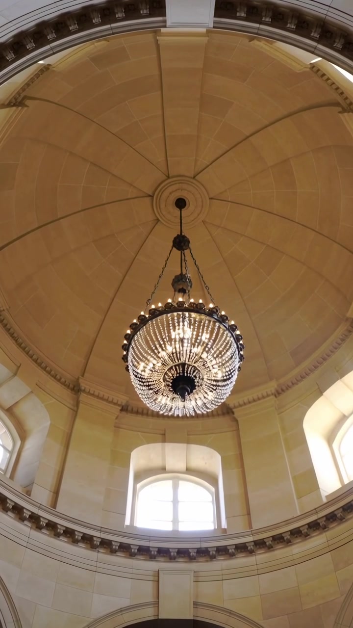 Video verticale: Telecamera che inclina e centra un lampadario di cristallo in una rotonda, con finestre ad arco retroilluminate.